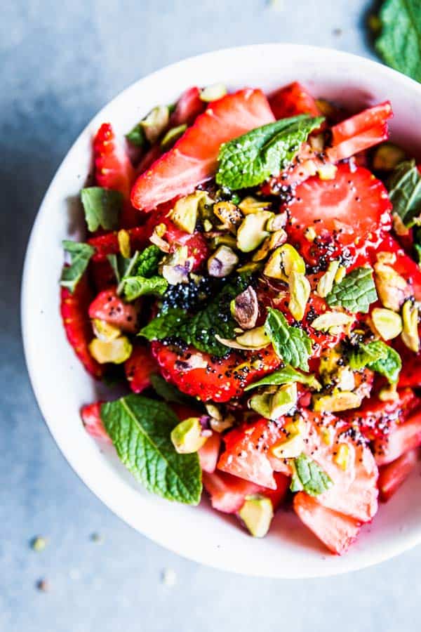 Strawberry Fruit Salad in a white bowl, sprinkled with pistachios and mint.