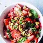 Strawberry Fruit Salad in a white bowl with mint leaves.