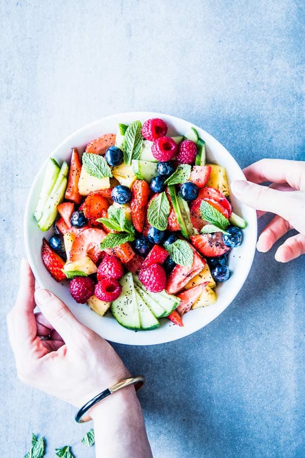 Woman placing a white bowl with summer fruit salad on the table.