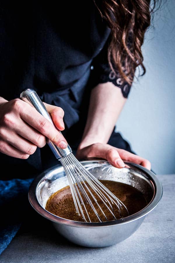 Woman in a black top whisking homemade teriyaki sauce.