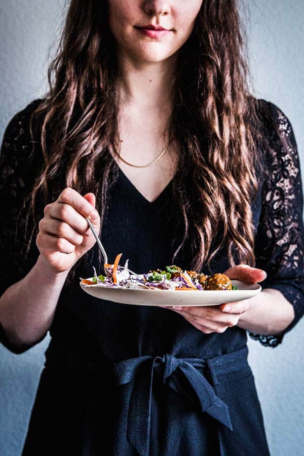 Woman in a black jumpsuit holding a plate with food.
