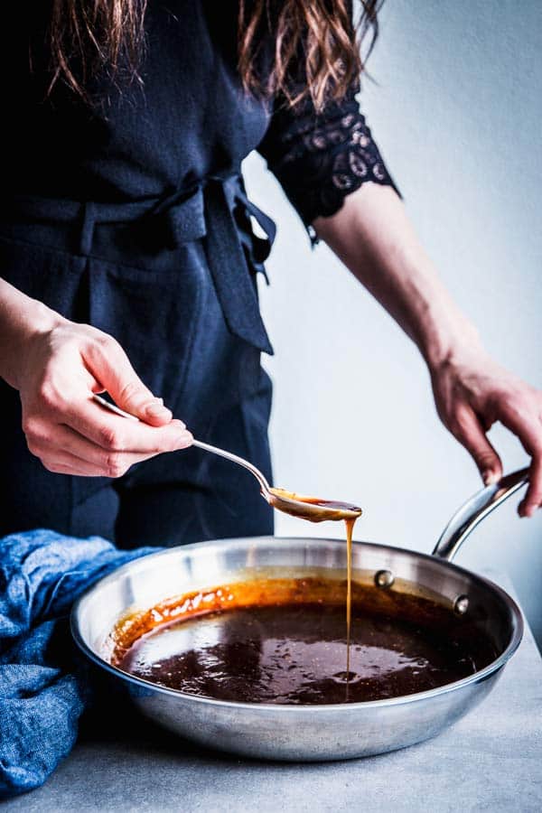 Woman in a black jumpsuit making teriyaki sauce.