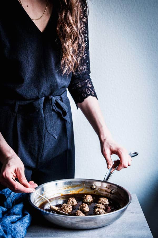 Woman in a black jumpsuit, adding meatballs to teriyaki sauce.