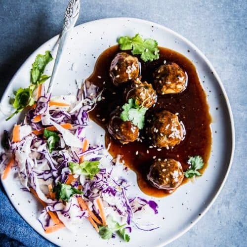 Teriyaki meatballs on a white plate with coleslaw.