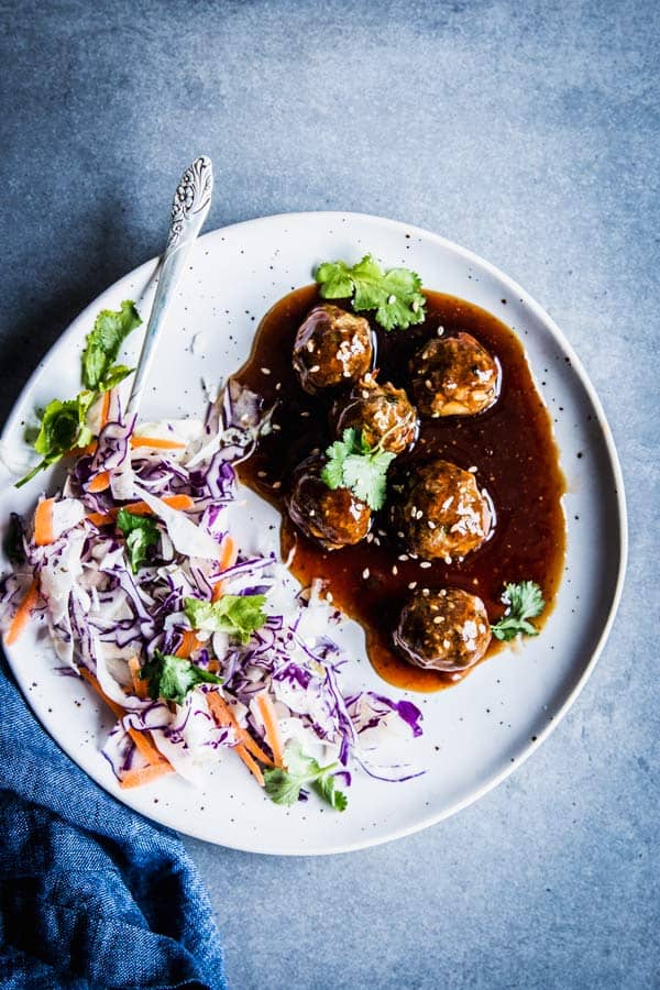 Teriyaki meatballs on a white plate with coleslaw.