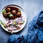 Teriyaki meatballs on a white plate with coleslaw, a fork and a dark napkin.