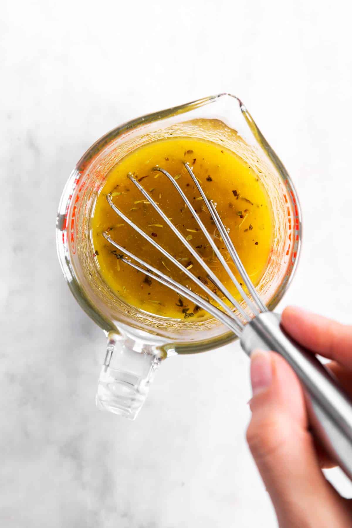 female hand whisking white balsamic vinaigrette in glass measuring jug