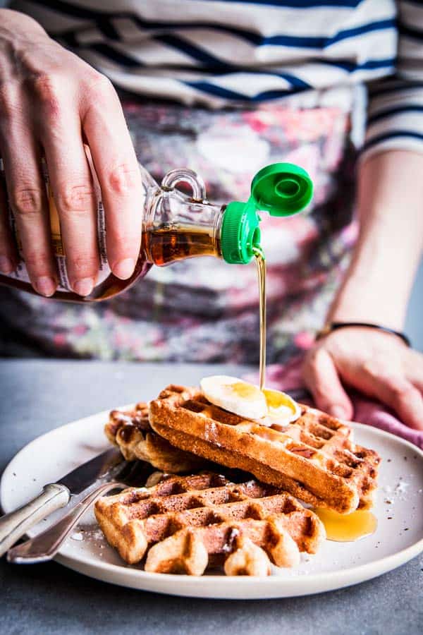 Woman in a striped top pouring maple syrup over banana nut waffles.