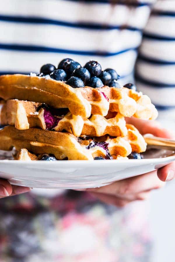 Woman in a striped shirt holding a plate with a stack of blueberry waffles.