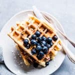 Blueberry waffles on a white plate with cutlery.