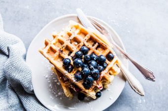 Blueberry waffles on a white plate with cutlery.