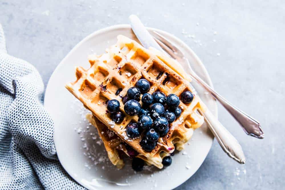 Blueberry waffles on a white plate with cutlery.