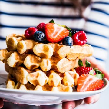 Woman in a striped shirt holding a plate with a stack of buttermilk waffles.