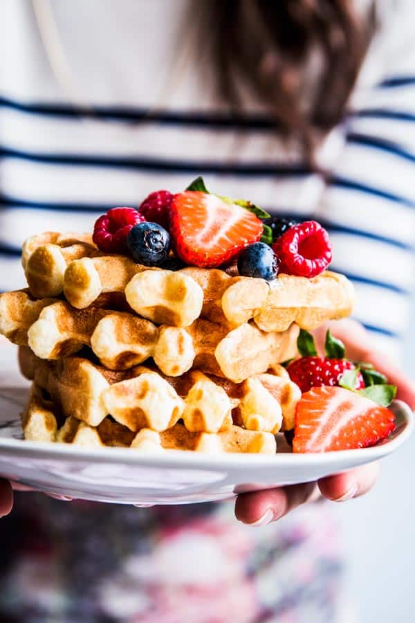 Woman in a striped shirt holding a plate with a stack of buttermilk waffles.