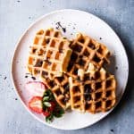 Chocolate chip waffles on a white plate with sliced strawberries.