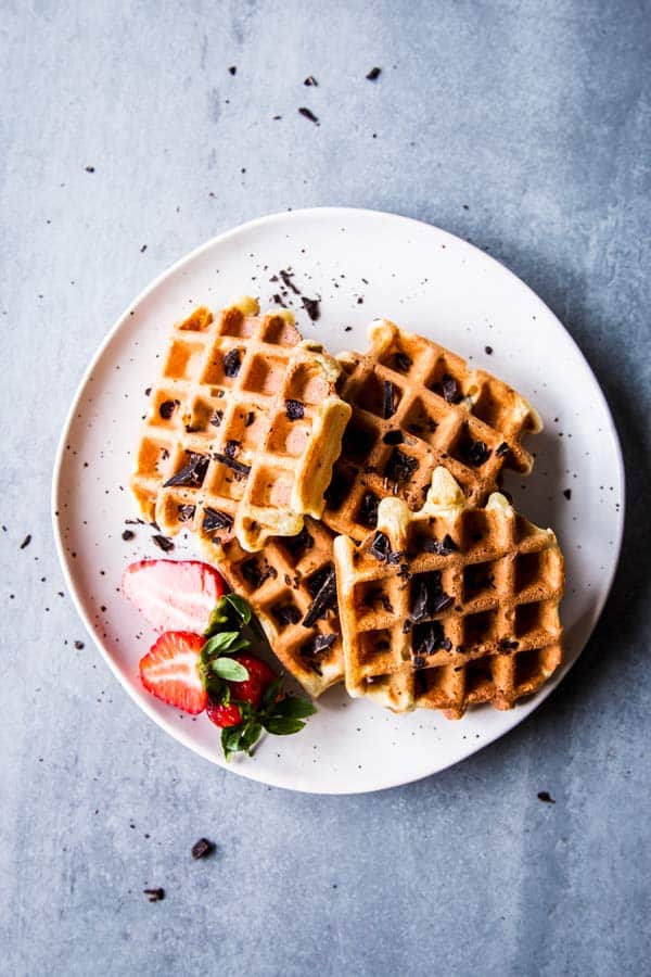 Chocolate chip waffles on a white plate with sliced strawberries.