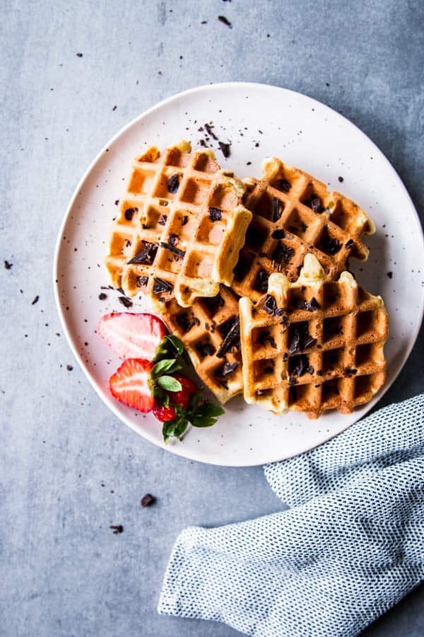 Chocolate Chip Waffles on a white plate with a light napkin and some strawberries.