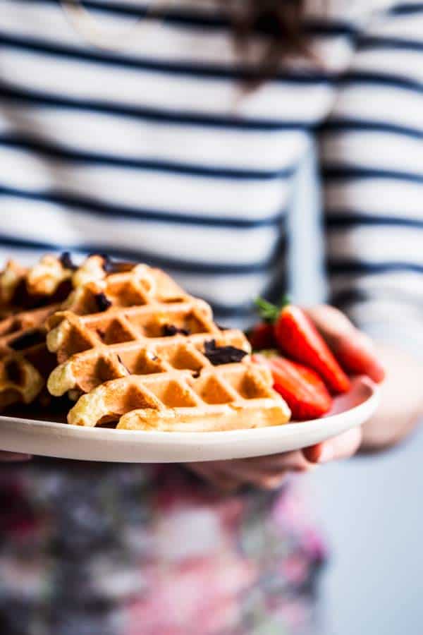 Woman in a striped shirt holding a plate with chocolate chip waffles.