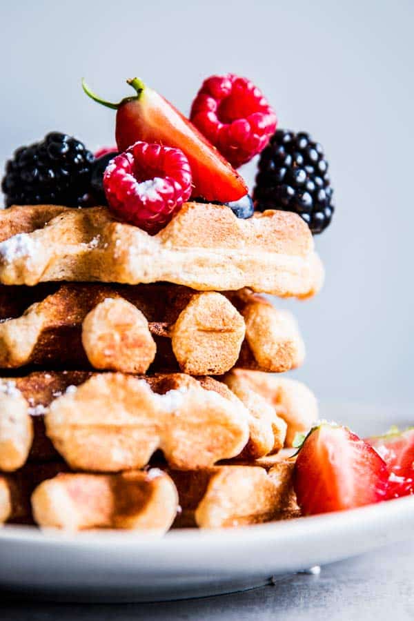 Stack of Fluffy Whole Wheat Waffles on a white plate, topped with fresh berries.