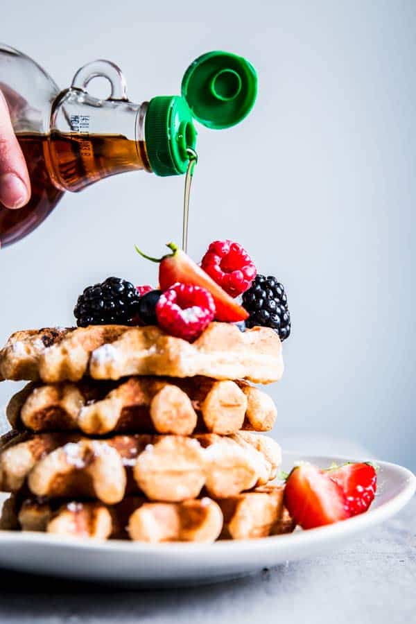 Pouring maple syrup over a stack of Fluffy Whole Wheat Waffles with berries.