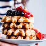 Woman in a striped shirt holding a plate with a stack of fluffy whole wheat waffles.