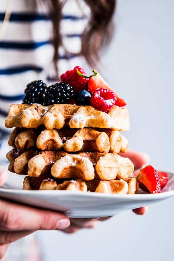 Woman in a striped shirt holding a plate with a stack of fluffy whole wheat waffles.