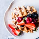 Fluffy Whole Wheat Waffles on a white plate with fresh berries.