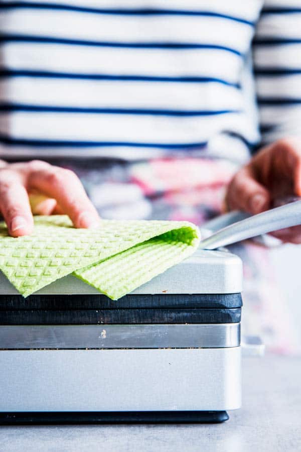 Wiping down a waffle maker with a green cloth.