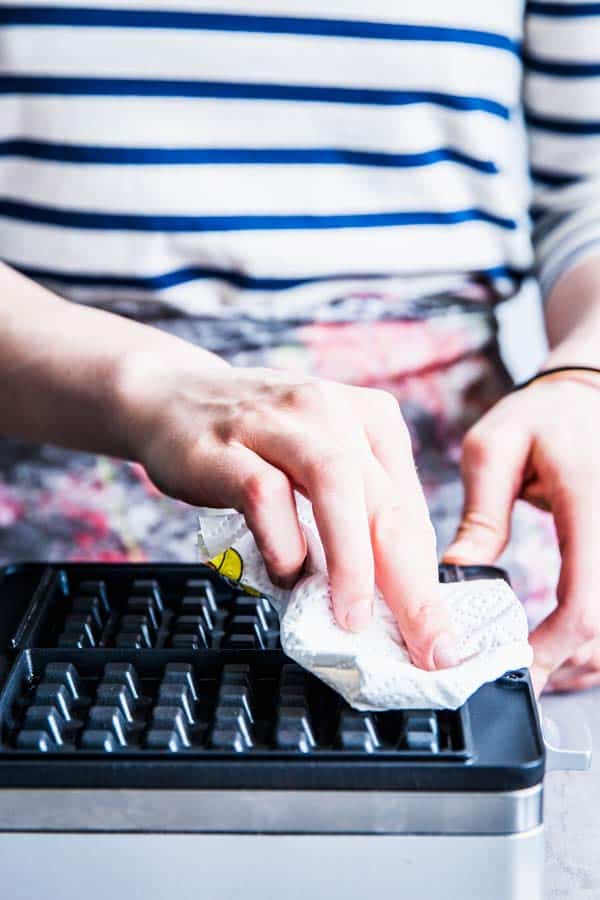 Woman in a striped shirt wiping down a waffle maker with a paper towel.