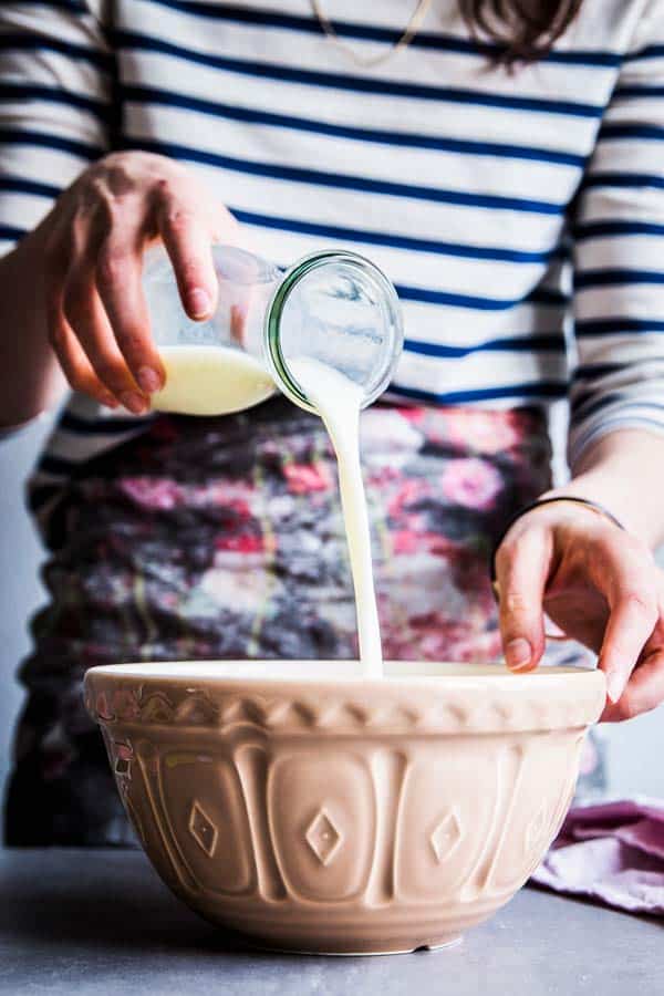 Woman in a striped top pouring buttermilk into batter for homemade waffles.