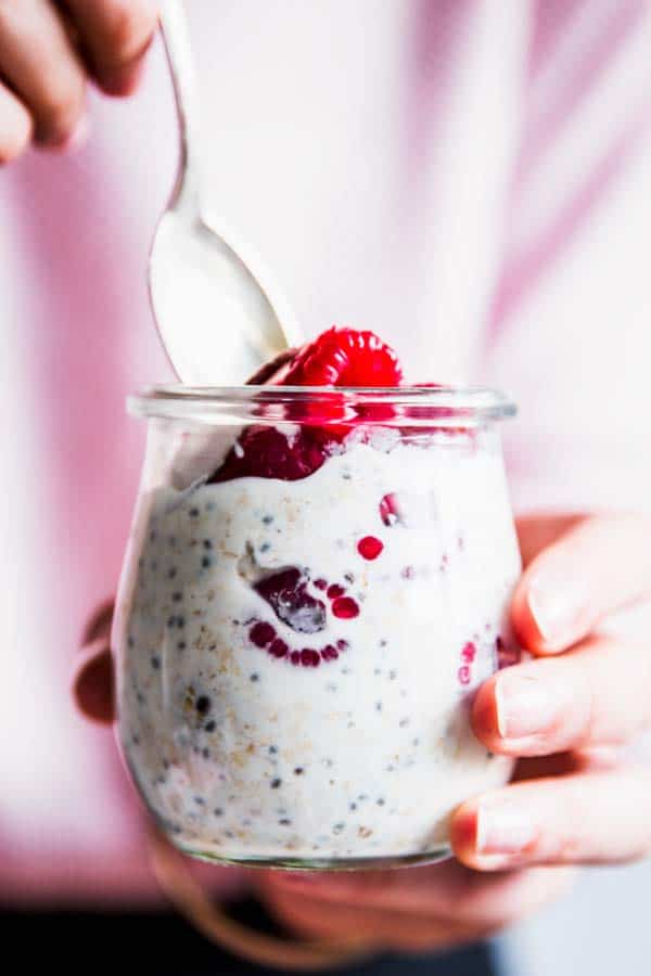 Woman eating raspberry coconut overnight oats from a jar.