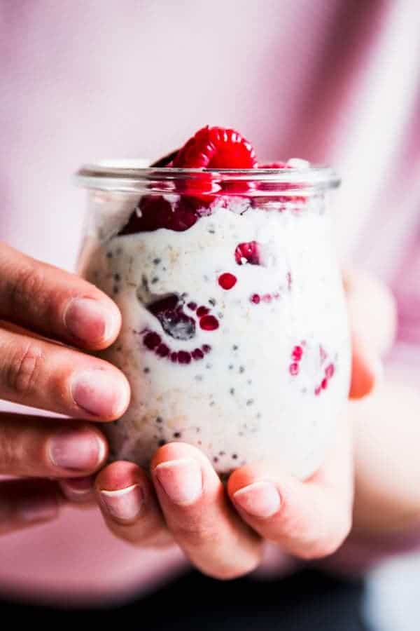 Woman holding a glass jar with raspberry coconut overnight oats.