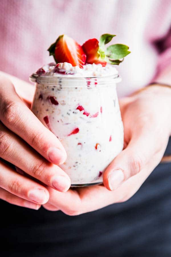 Woman holding a jar of vanilla strawberry overnight oats.