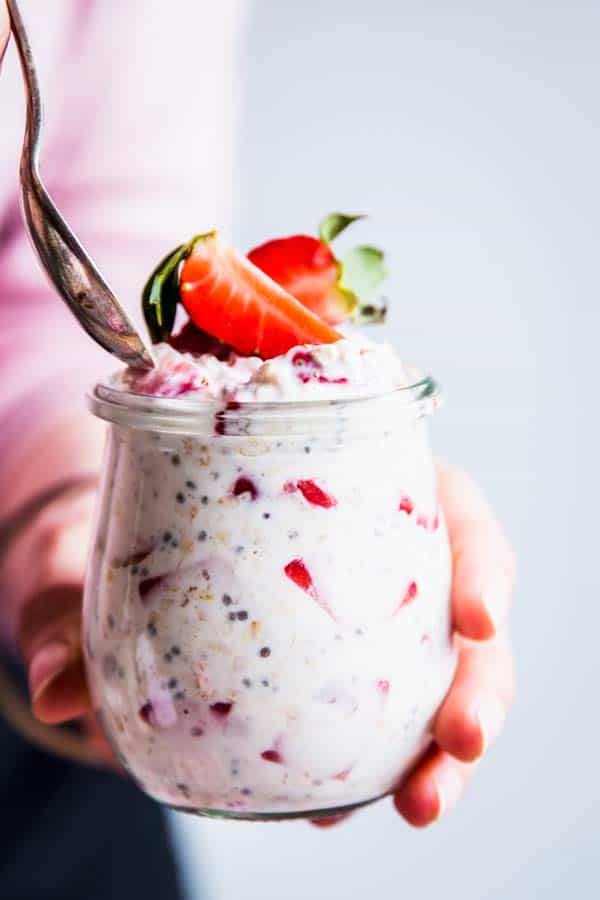 Spooning Vanilla Strawberry Overnight Oats from a small glass jar.