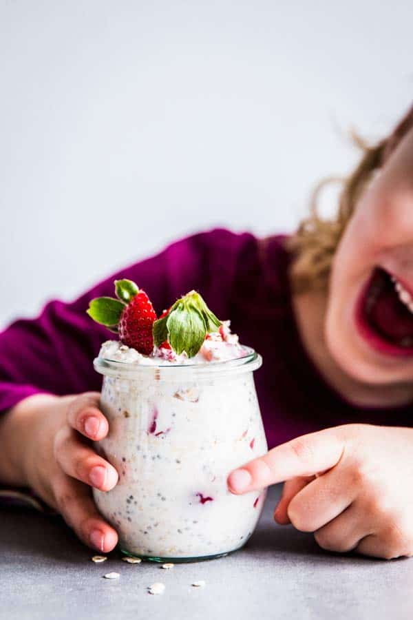 Girl with strawberry overnight oats in a jar.