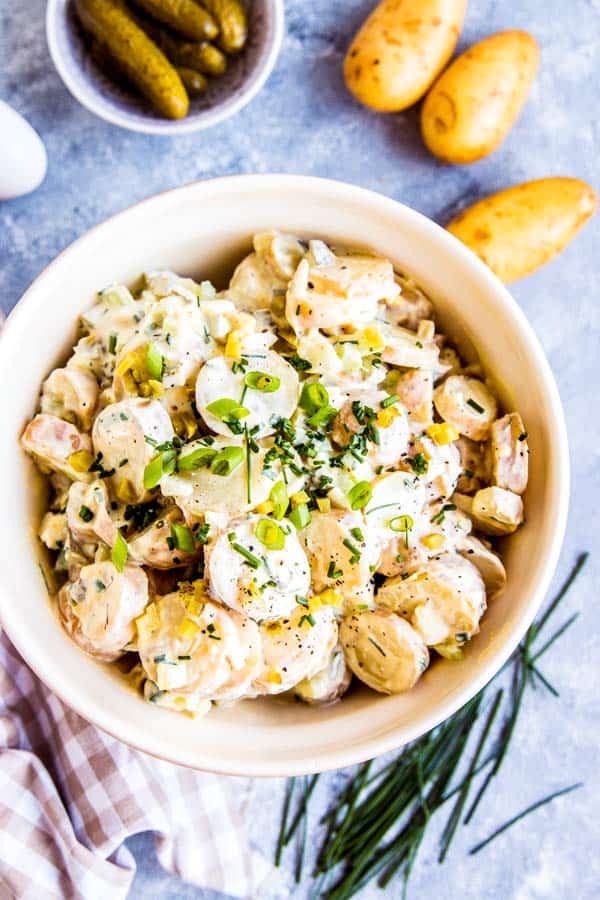 cream greek potato salad in a bowl with ingredients around it