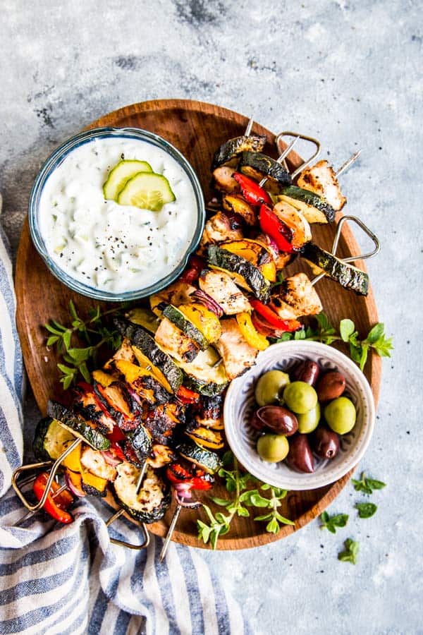 greek chicken kabobs on a wooden platter with tzatziki and olives