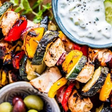 greek chicken kabobs on a platter with tzatziki and olives