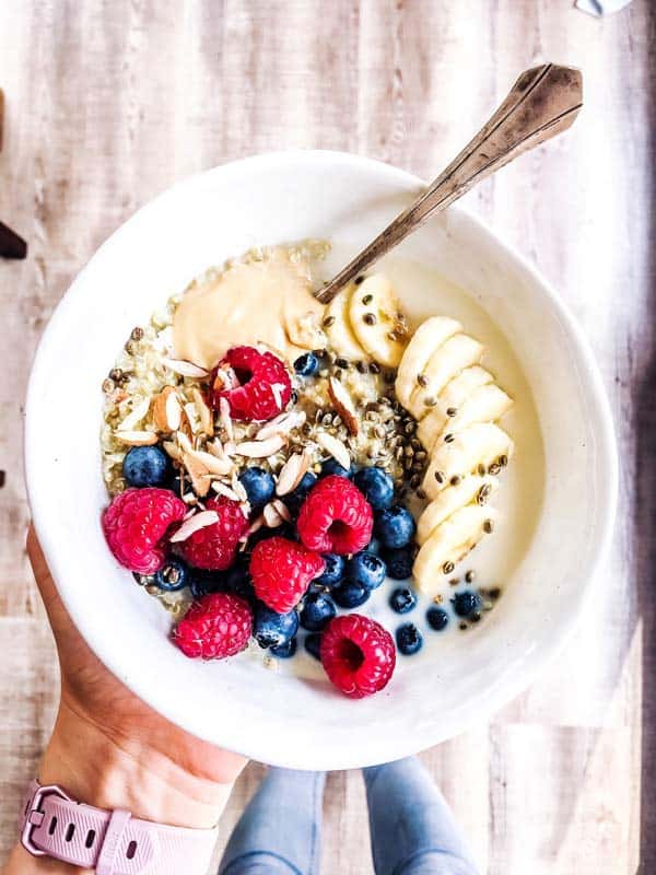 woman holding a white bowl with breakfast quinoa and berries