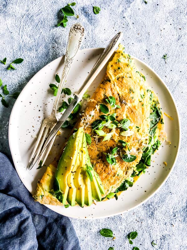 green goddess omelette on a white plate with herbs and avocado
