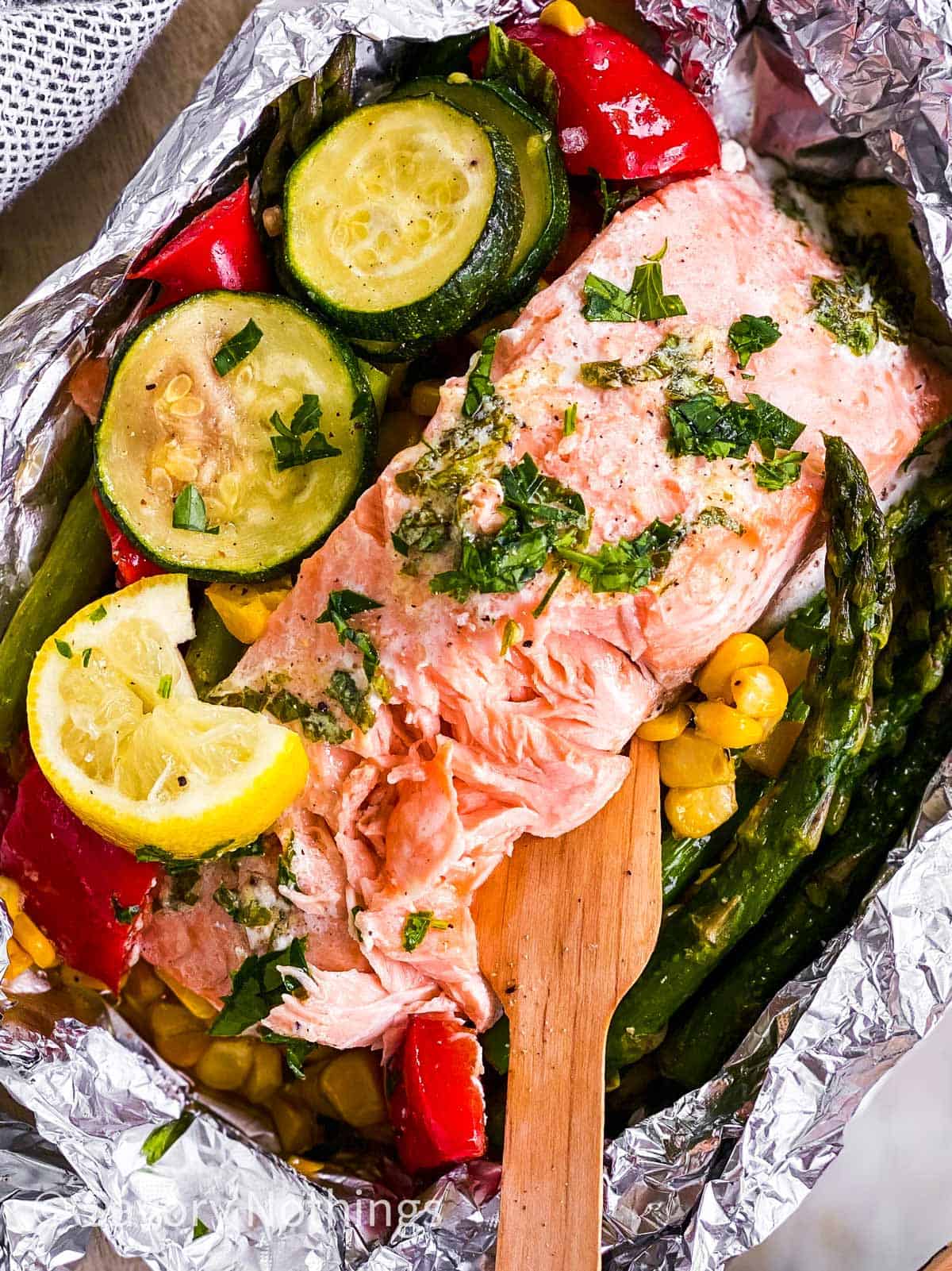 close up photo of flaked salmon in foil pouch with summer vegetables and wooden fork