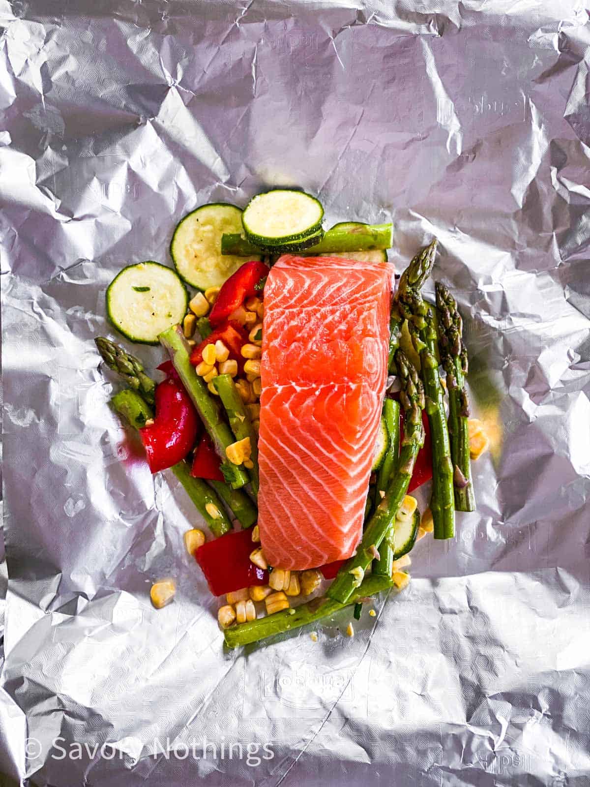 vegetables and raw salmon fillet on piece of aluminium foil