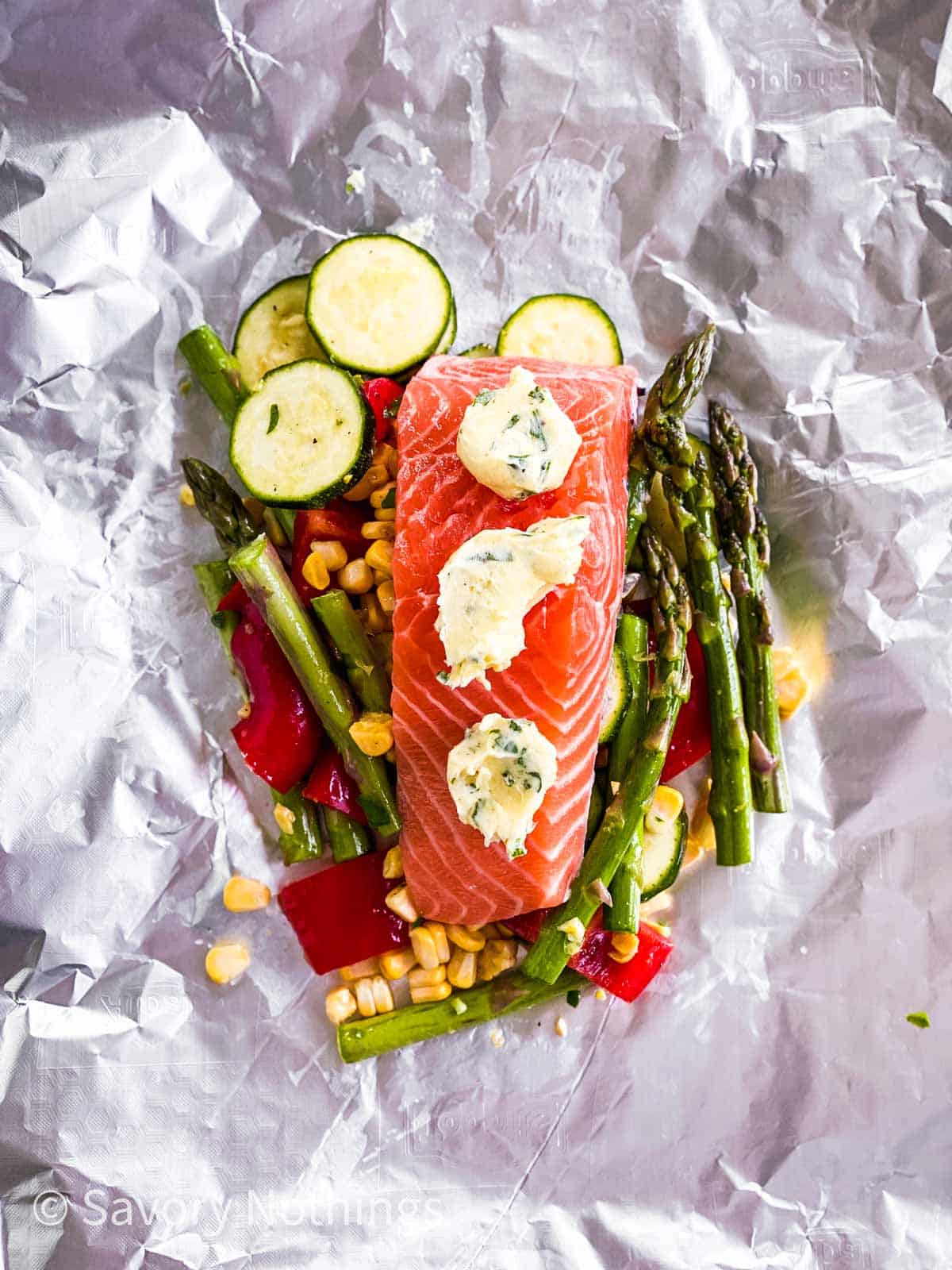 vegetables and raw salmon fillet on piece of aluminium foil topped with garlic herb butter