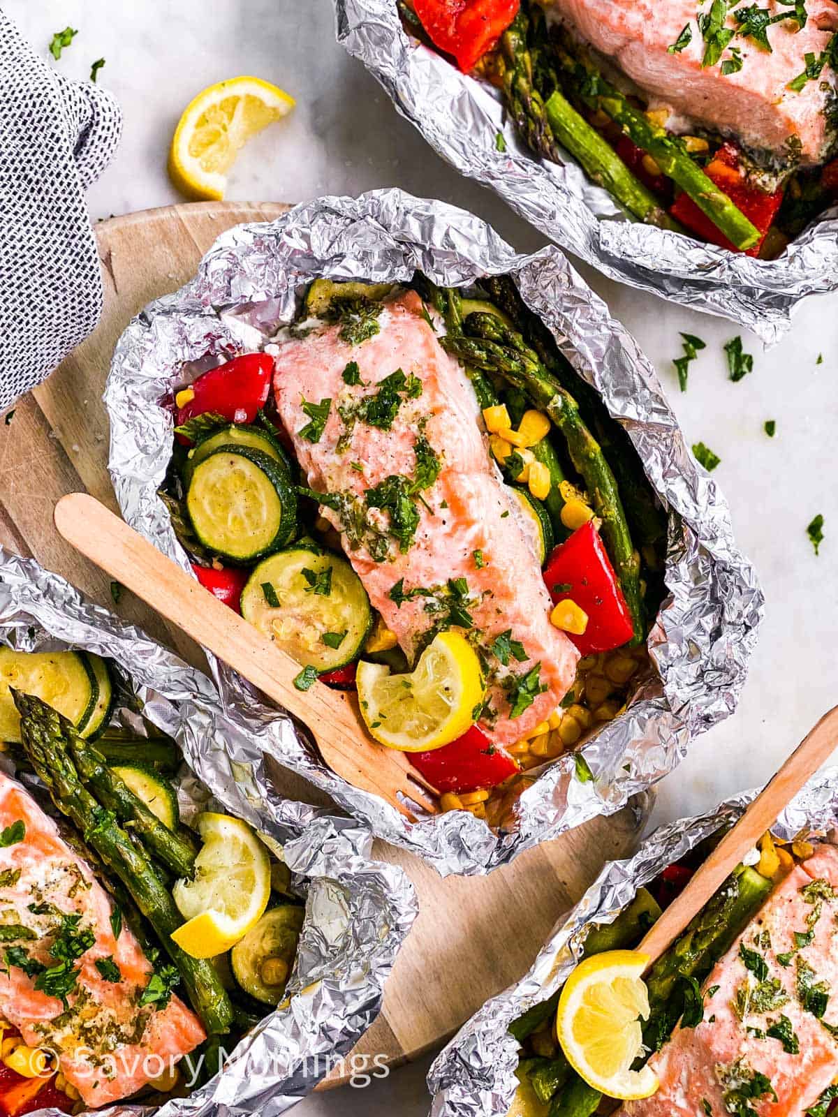 overhead view of four opened salmon foil packets garnished with fresh lemon and chopped parsley