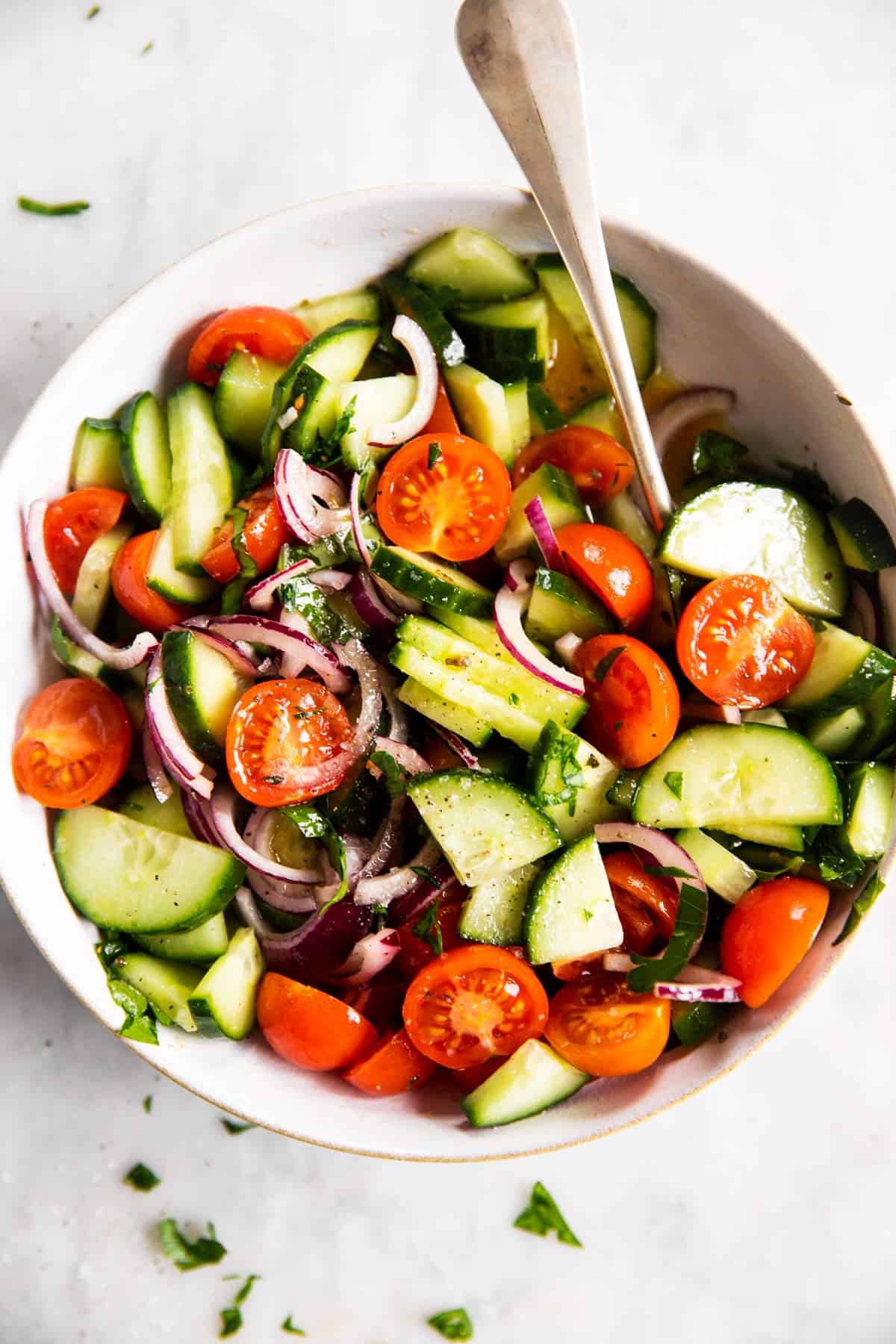 white bowl with tomato cucumber salad on marble surface