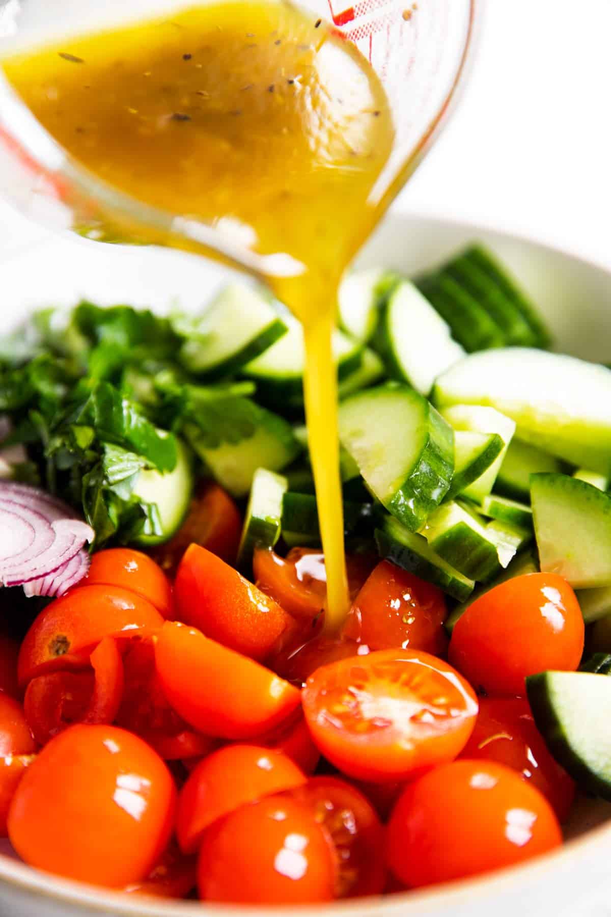 pouring dressing over cucumbers and tomatoes in bowl