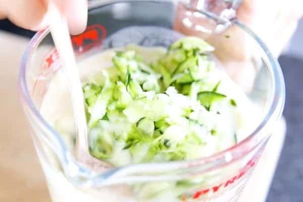 stirring shredded zucchini into wet ingredients for zucchini bread