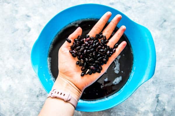 holding black beans over a blue bowl