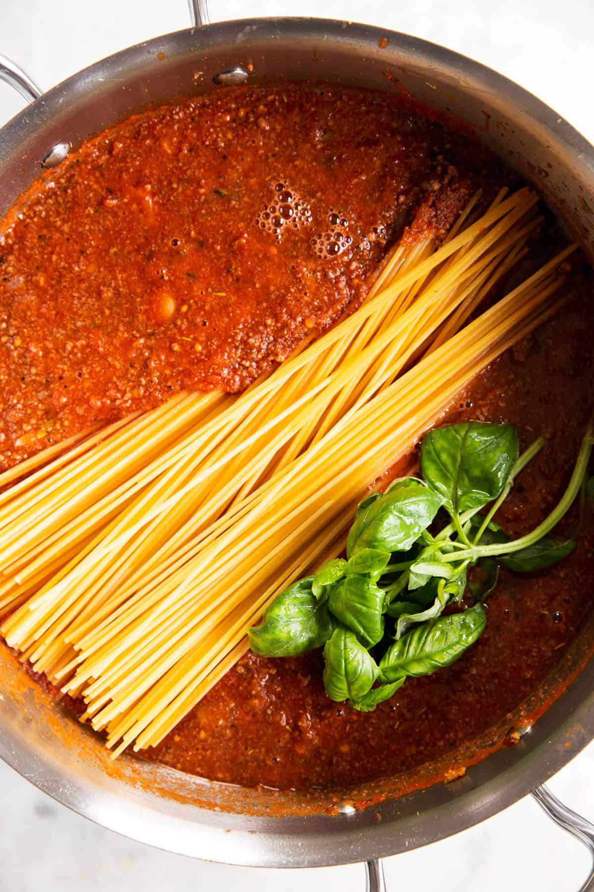 overhead view of raw spaghetti in meat sauce with basil in skillet