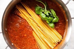 overhead view of raw spaghetti in meat sauce with basil in skillet